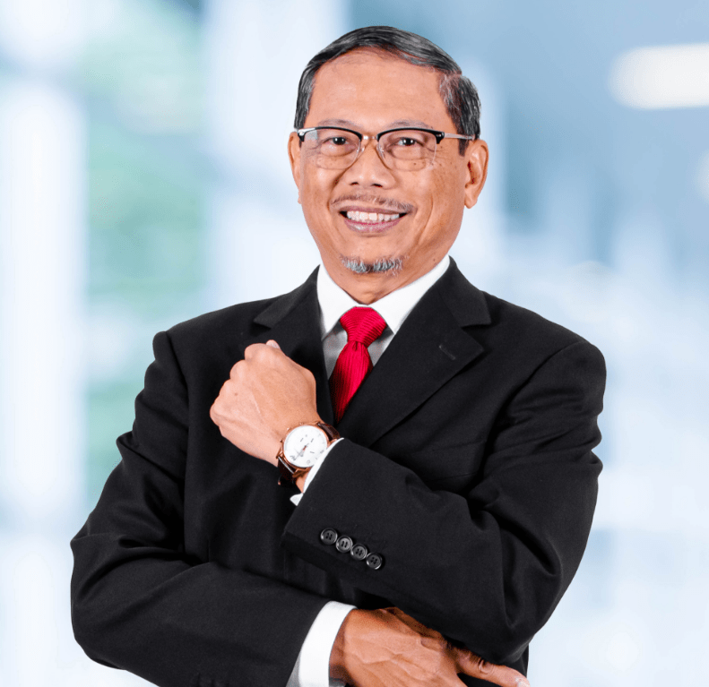 a man wearing a black suit, white shirt, and red tie, with his left hand adjusting his right sleeve cuff while wearing a wristwatch. The background appears to be a blurred office setting