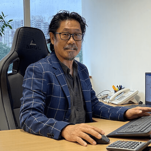 a person in a checkered suit sitting at an office desk, working on a computer with a black office chair and a telephone in the background