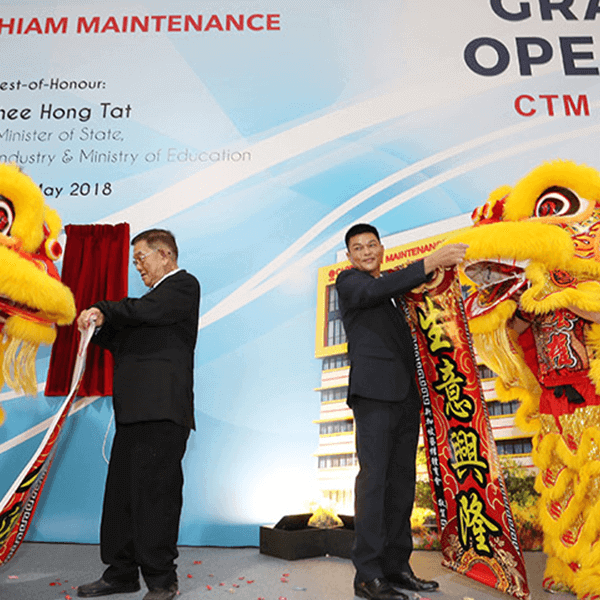 two individuals in a ribbon-cutting ceremony with large golden lion dance costumes presented on the right