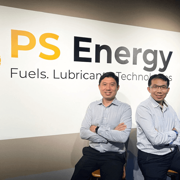 two individuals in light blue shirts standing with arms crossed in front of a wall with the "PS Energy" logo and the words "Fuels. Lubricants. Technologies" written underneath