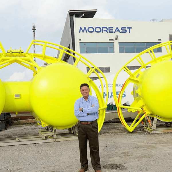 a person stands with crossed arms in front of large, bright yellow spherical structures with protruding frames