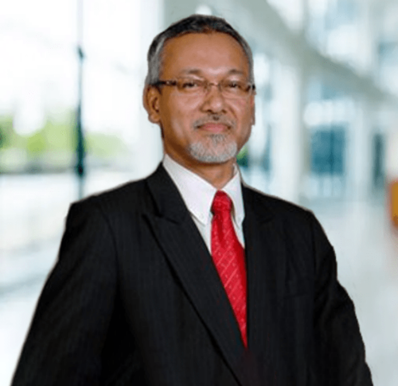 a man dressed in a professional black suit with a white shirt and red tie, standing in a lobby with blurred background