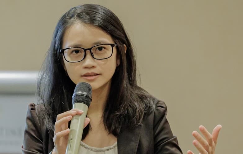 a woman wearing glasses speaks into a microphone, conveying her message with confidence and clarity